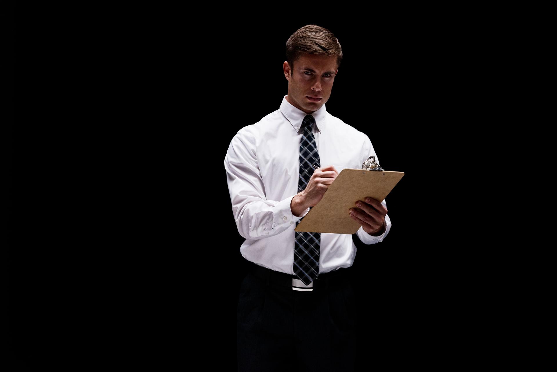 Caucasian male businessman in front of black background wearing businesswear and holding to do list